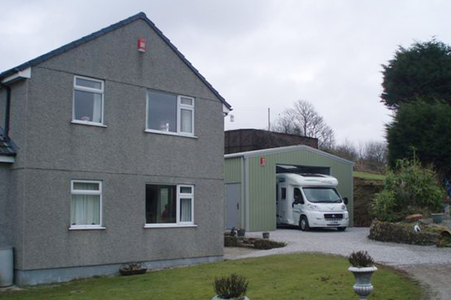 A two-storey house next to a green building containing a motorhome