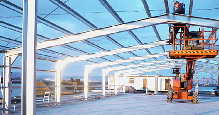 A man on a cherry picker is inspecting the steel framework of a building under contruction