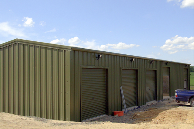 A green building with multiple closed roller doors and one slightly larger open roller door